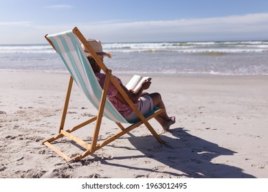 Senior african american woman reading a book while sitting on deck chair at the beach. travel vacation retirement lifestyle concept - Powered by Shutterstock