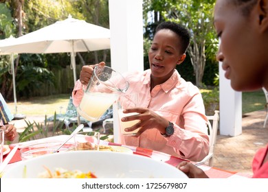 Senior African American woman spending time with his family in the garden on a sunny day, sitting by a table pouring lemonade to a glass. - Powered by Shutterstock