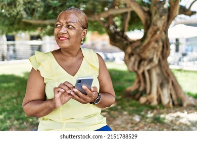 Senior african american woman using smartphone sitting on the bench at the park. - Powered by Shutterstock