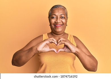 Senior african american woman wearing casual style with sleeveless shirt smiling in love doing heart symbol shape with hands. romantic concept. 