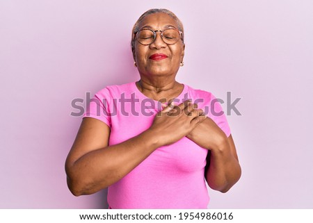 Senior african american woman wearing casual clothes and glasses smiling with hands on chest with closed eyes and grateful gesture on face. health concept. 