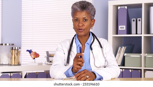 Senior African Doctor Sitting At Desk And Talking To Camera