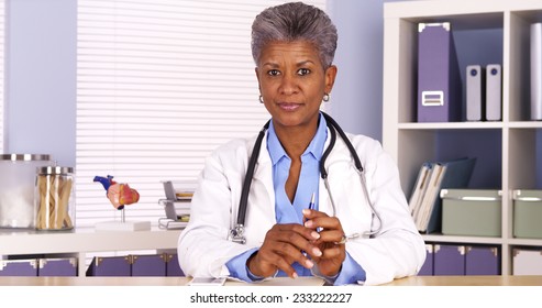 Senior African Doctor Sitting At Desk And Talking To Camera