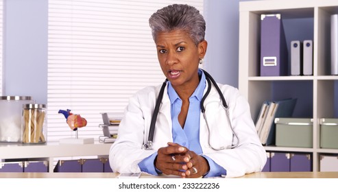 Senior African Doctor Sitting At Desk And Talking To Camera