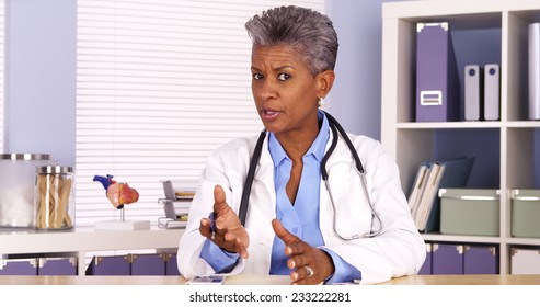 Senior African Doctor Sitting At Desk And Talking To Camera