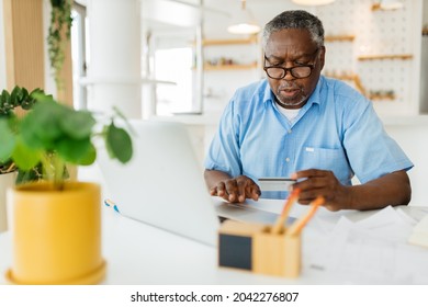 Senior African man sitting in his home office with credit card in hand and using laptop for paying bills. E banking concept. - Powered by Shutterstock