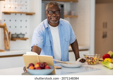 Senior African man standing in the kitchen, reading recipe in book and preparing a healthy meal. - Powered by Shutterstock