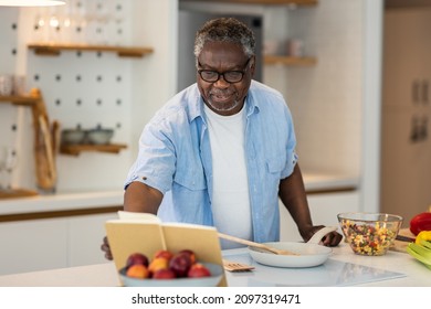 Senior African man standing in the kitchen, reading recipe in book and preparing a healthy meal. - Powered by Shutterstock