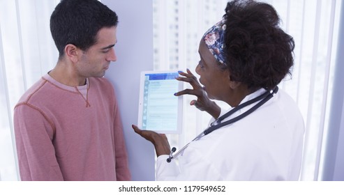 Senior African MD Showing Male Latino Patient Different Health Plans On Tablet