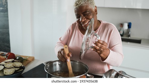 Senior african woman cooking dinner at home inside kitchen - Food and real people concept - Main focus on face