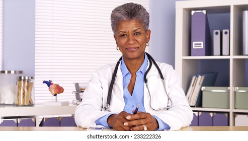 Senior African Woman Doctor Sitting At Desk And Talking To Camera