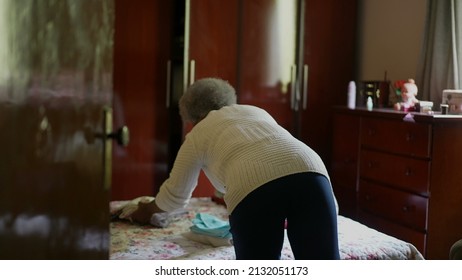 A Senior African Woman Tidying Up Room Removing Clothes From Bed Organizing Housework