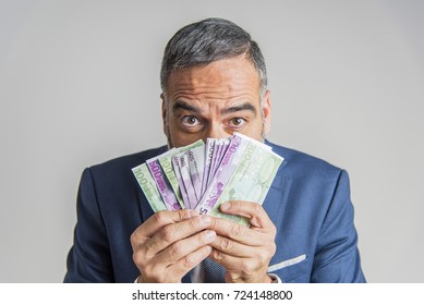 Senior Aged Businessman Hiding Behind A Stack Of Euro Bills, Making A Silly Goofy Face