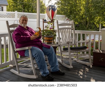 A Senior Aged Male Resting in a Rocking Chair, on a Deck, Enjoying His Retirement Wondering What He is Holding, on a Autumn Day