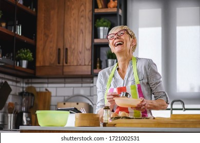 Senior Aged Woman Baking In Home Kitchen. Using Tablet Computer To Find Recipe. Mature Woman Cooking With The Help Of Internet. Modern Technology For Older People.