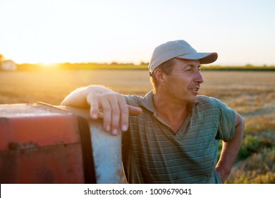 Senior agronomist man standing in a field leaning against old tractor after harvest at sunset. - Powered by Shutterstock