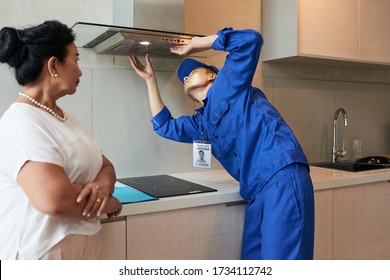 Senior apartment owner looking at service worker checking broken cooker hood