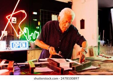 A senior artisan works on a neon sign in a workshop, using a torch to bend and shape the glass tubing. - Powered by Shutterstock