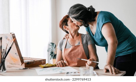 Senior artist gay couple painting watercolor canvas at art home workshop - LGBTQ Lesbian mature women kissing - Small family business concept - Powered by Shutterstock