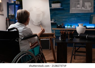 Senior artist using wheelchair drawing original pencil artwork of still life vase feeling creative on easel in home studio. Older woman who is paralyzed creating authentic design sketch in workshop. - Powered by Shutterstock