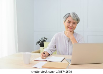 Senior Asia Woman Working From Home Using Laptop And Smart Phone. Old Woman Living And Learning Online.