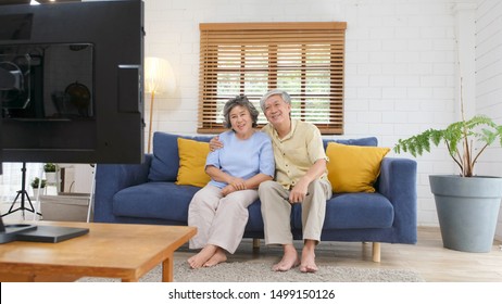 Senior Asian, 60s, Couple Holding Remote Control While Watching Television In Home Living Room With Happiness, Old People Retirement Routine Lifestyle