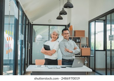 Senior Asian business woman and young man working together analyzing finances senior staff teach marketing and planning to younger staff woman holding graph and chart with a happy smile - Powered by Shutterstock