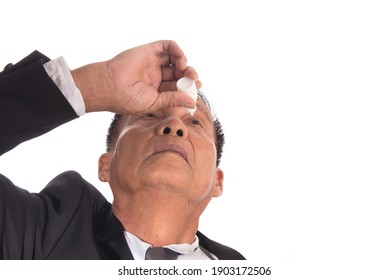 Senior Asian Businessman Getting The Medicine In The Eye. Older Man Applying Eye Drops Isolated On White Background. Man Putting Liquid Drops In His Eye Solving Vision Problem.