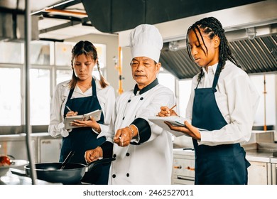 Senior Asian chef educates diverse students in a restaurant kitchen. Stressing teamwork learning and note-taking in this professional educational setting. Food Edocation - Powered by Shutterstock