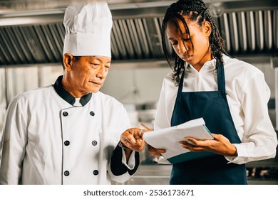 Senior Asian chef professionally teaching diverse students cooking in a restaurant kitchen workshop. Emphasizing teamwork learning and note-taking in this educational setting. Food Edocation - Powered by Shutterstock