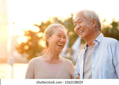 senior asian couple enjoying good time outdoors in park at dusk, happy and smiling