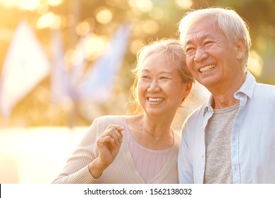 Senior Asian Couple Enjoying Good Time Outdoors In Park At Dusk, Happy And Smiling