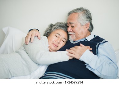 Senior Asian Couple Love Lying On The Bed With Hug And Hold The Hand. Retired Man And Woman Sleeping With Talking On Bed In Bed Room At Home Which Smiling And Felling Happy. Old Couple Love Concept