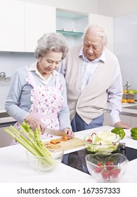 senior asian couple preparing meal together in kitchen.