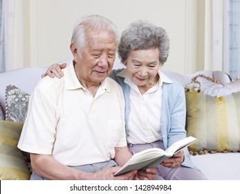 Senior Asian Couple Reading A Book Together At Home.