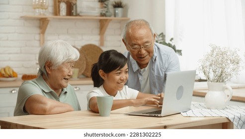 Senior asian couple together with their teen granddaughter who teaches them how to use a laptop, surfing through internet - family bonds and ties concept  - Powered by Shutterstock