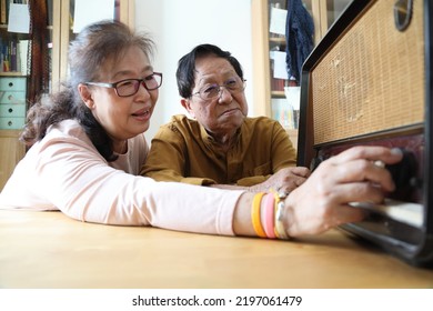 The Senior Asian Couple Trying To Listen Music From The Vintage Radio.