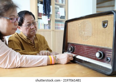 The Senior Asian Couple Trying To Listen Music From The Vintage Radio.