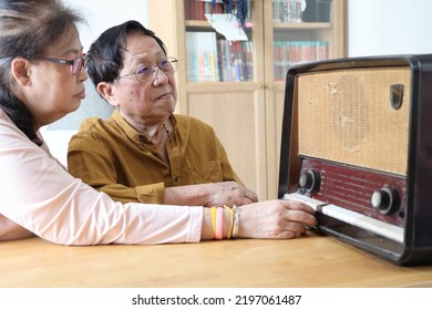 The Senior Asian Couple Trying To Listen Music From The Vintage Radio.