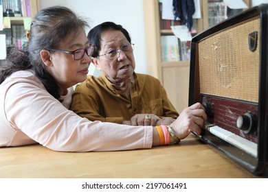 The Senior Asian Couple Trying To Listen Music From The Vintage Radio.