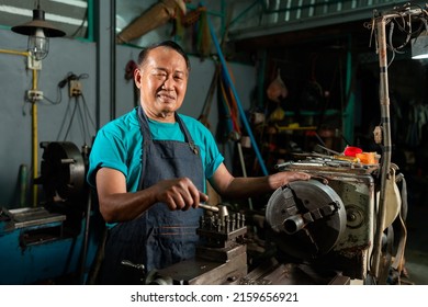 A Senior Asian Craftsman, Standing Closely And Carefully Controlling A Lathe, Inside A Small Factory Of His Family Business.