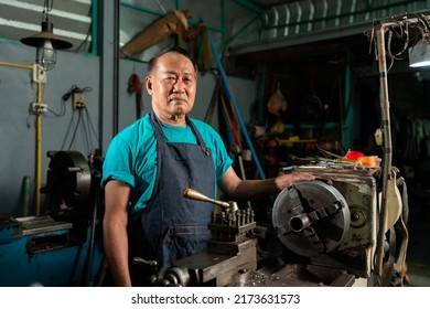 A Senior Asian Craftsman, Standing Closely And Carefully Controlling A Lathe, Inside A Small Factory Of His Family Business..