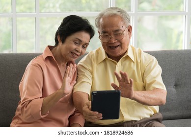 Senior Asian Elderly Couple In Home Casual Outfit Sitting In Living Room Using Smart Tablet To Video Call Facetime With Family