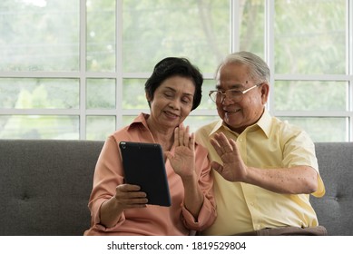 Senior Asian Elderly Couple In Home Casual Outfit Sitting In Living Room Using Smart Tablet To Video Call Facetime With Family