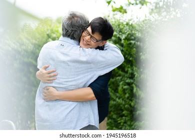 Senior Asian Father With Adult Grown Son Hugging Outdoors.