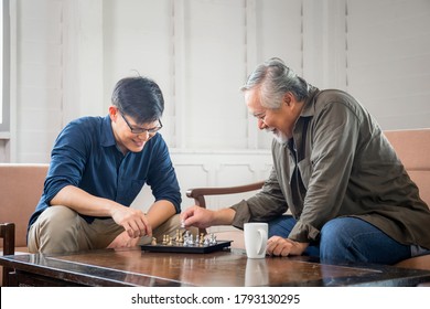 Senior Asian Father And Middle Aged Son Playing Chess Game In Living Room, Happiness Asian Family Concepts