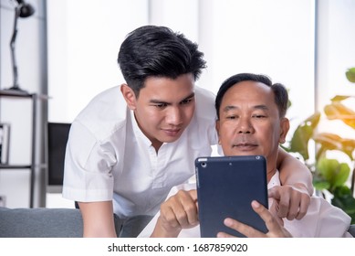 Senior Asian Father And Son Are Discussing The Popular Online Business Investment On Smartphones. Warmly In The Morning At Home The Concept Of Family Life