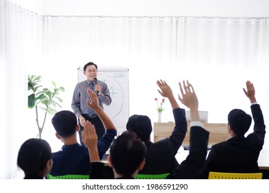 Senior Asian Lecturer is lecturing about business and stock market topics and business people are having a seminar and raising hands agree with teacher in the economics class in meeting room.