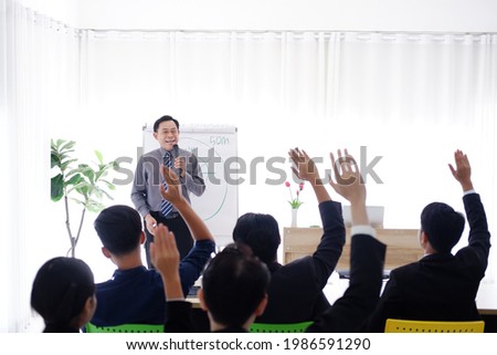 Senior Asian Lecturer is lecturing about business and stock market topics and business people are having a seminar and raising hands agree with teacher in the economics class in meeting room.