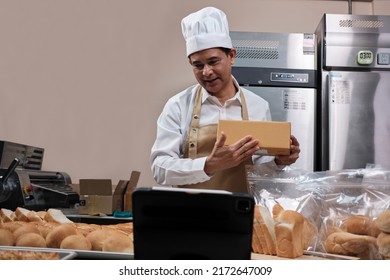 Senior Asian Male Chef In Apron, Small Business Blogger Live Streaming Via Mobile Application Technology, Bakery Sales Online Promotion, Fresh Bread, Pastry Food, And Commercial Cooking In Kitchen.